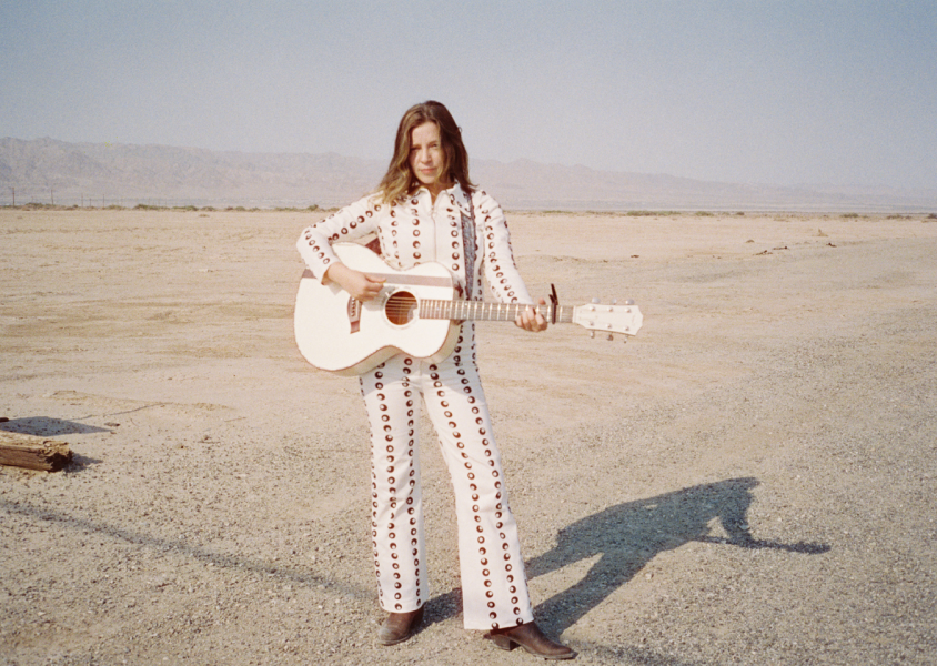 Artist Jade Bird standing with guitar in desertx